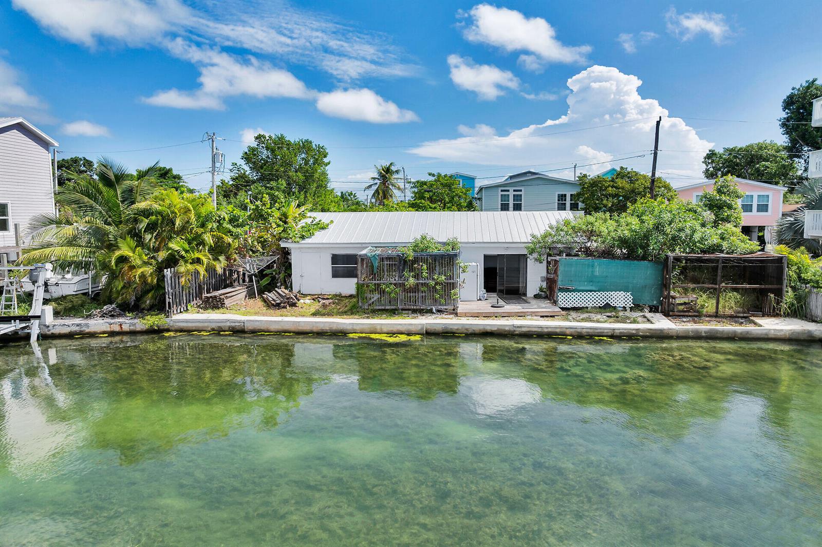 A white house with a metal roof sits along a canal with a seawall — 4 Shore Drive, Key West FL 33040, KEY WEST, FL