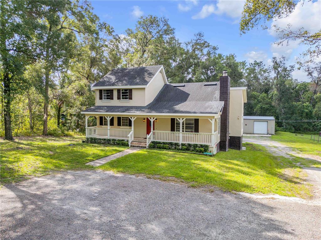 A two-story house with a front porch, stone chimney, and detached garage on a wooded lot — 1080 E FRENCH AVENUE, ORANGE CITY, FL