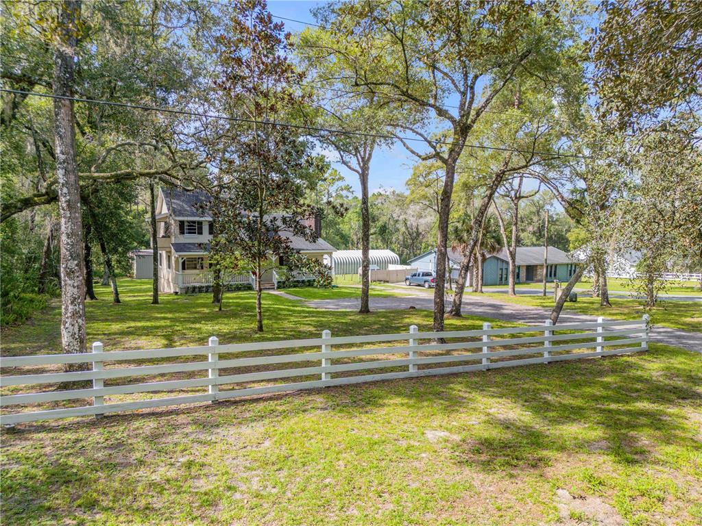 A white fence stands in front of a two-story house with a porch and trees — 1080 E FRENCH AVENUE, ORANGE CITY, FL