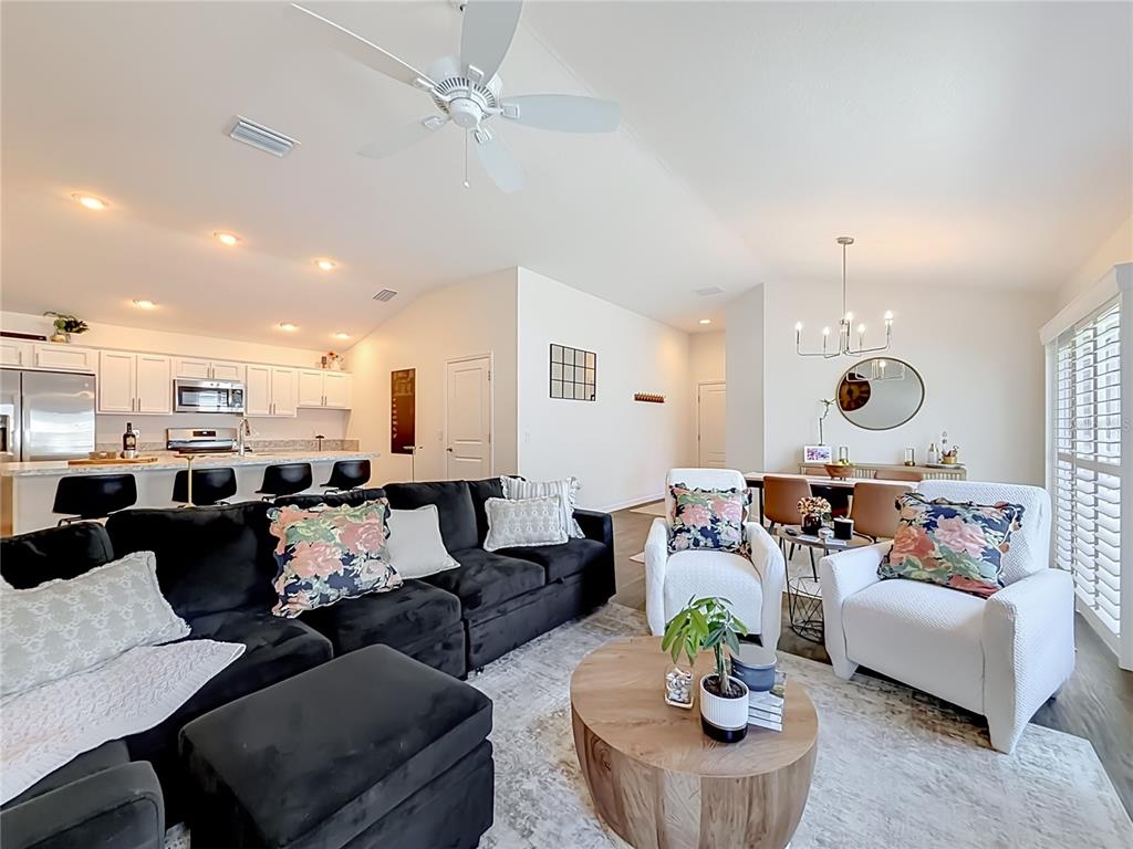 An open-concept living area features a black sectional sofa, white armchairs, and a kitchen island — 6231 ATKINSON LANE, THE VILLAGES, FL