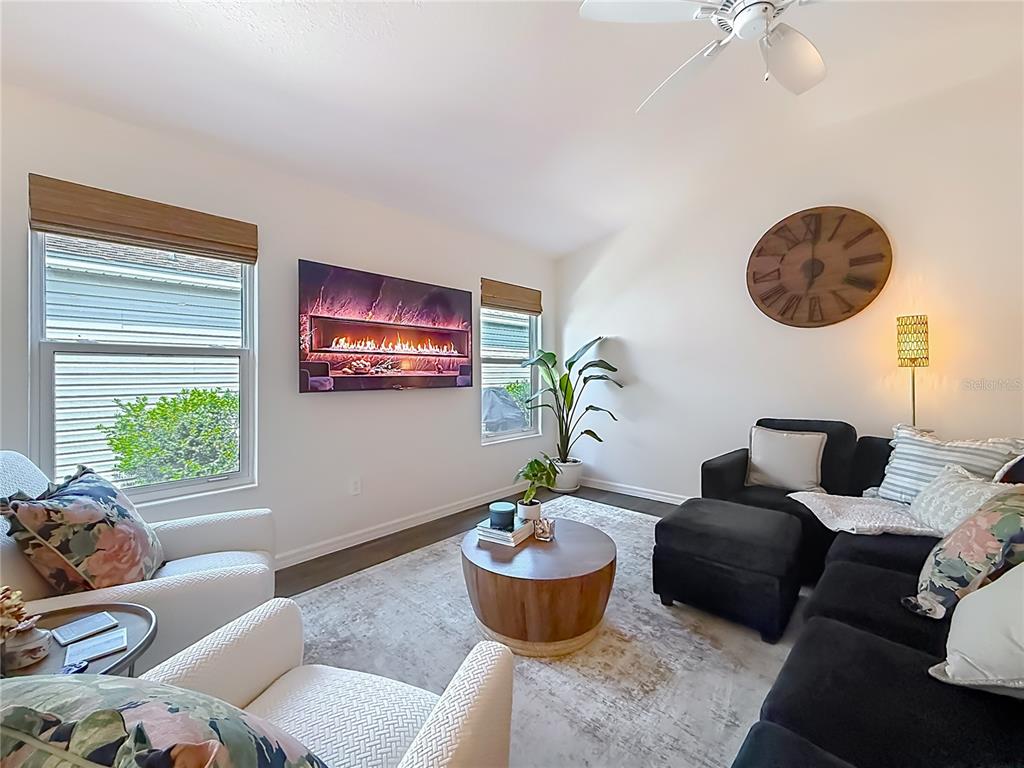 A living room features a wall-mounted electric fireplace, a dark sectional, and two armchairs — 6231 ATKINSON LANE, THE VILLAGES, FL