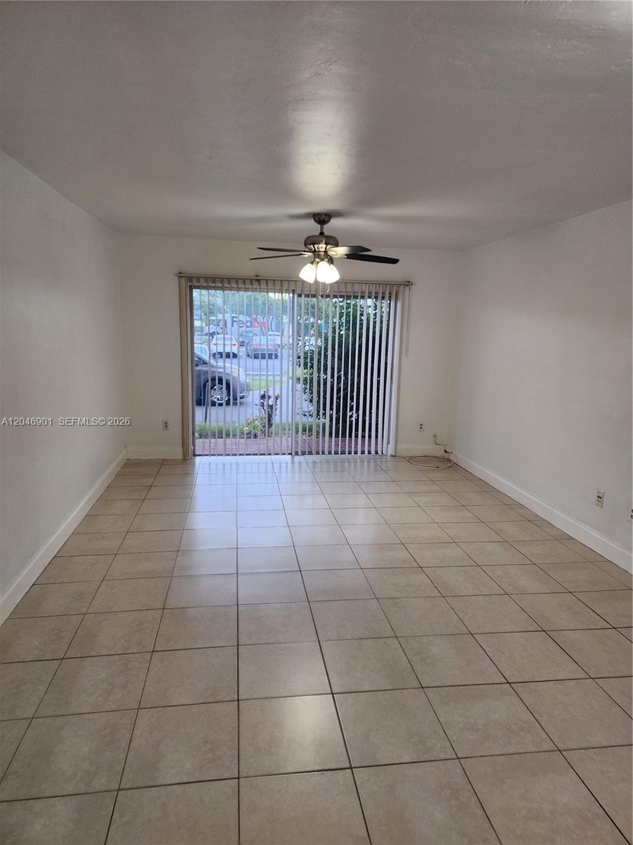 An empty room features beige tile flooring, white walls, a ceiling fan, and sliding glass doors — MIAMI, FL