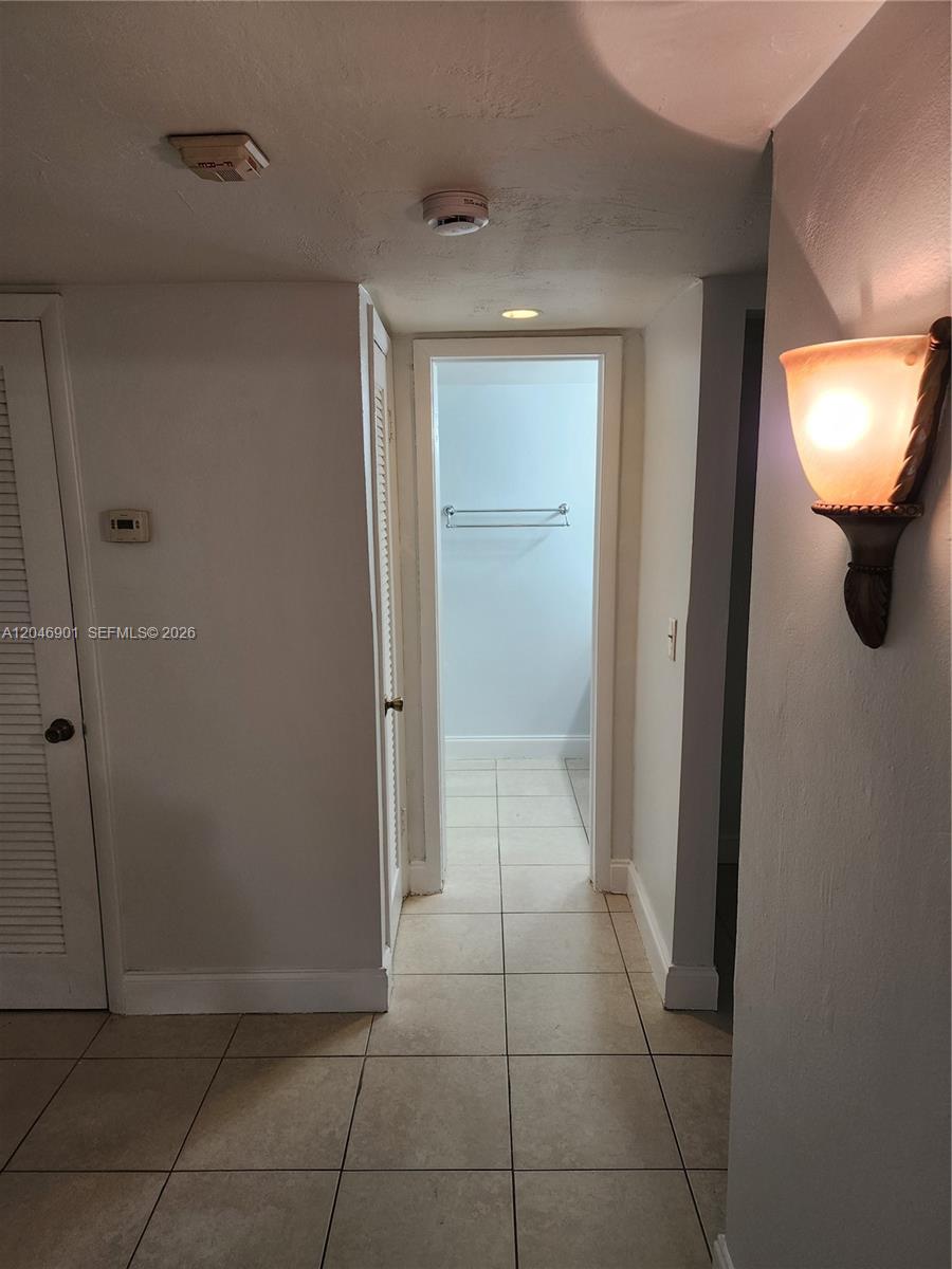 A hallway with tiled floors leads to a bathroom featuring a towel rack — MIAMI, FL