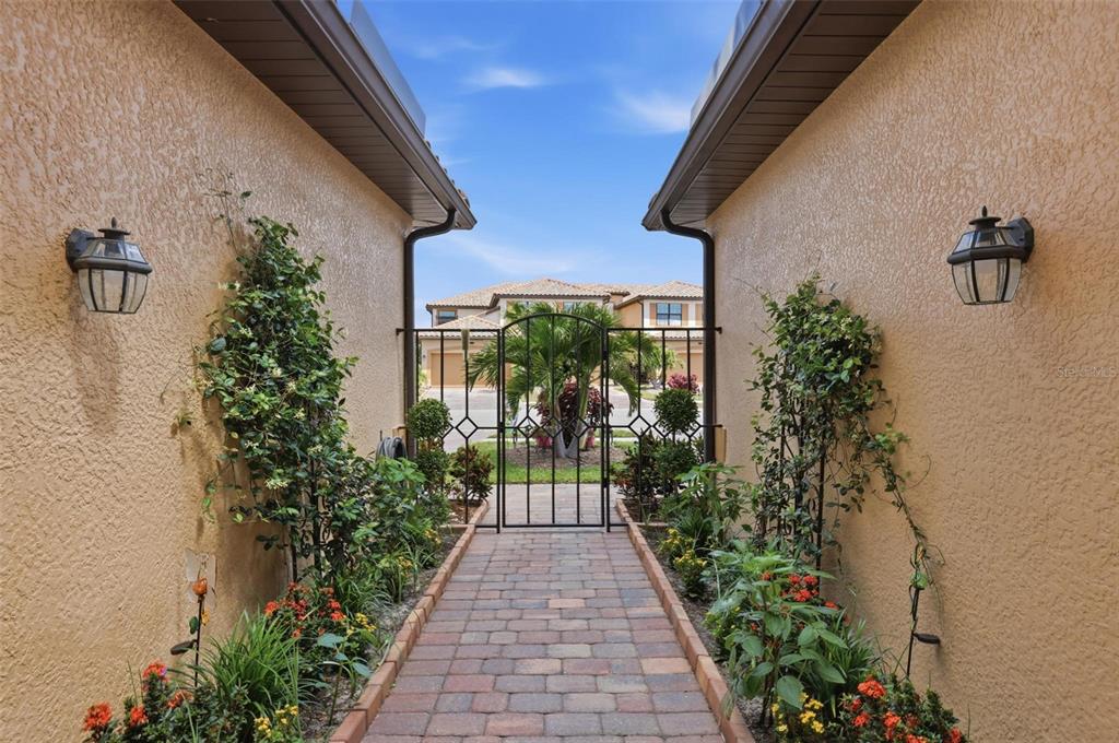 A brick walkway leads through a gated courtyard between two stucco walls with wall lanterns — 20120 RAGAZZA CIRCLE UNIT 202, VENICE, FL