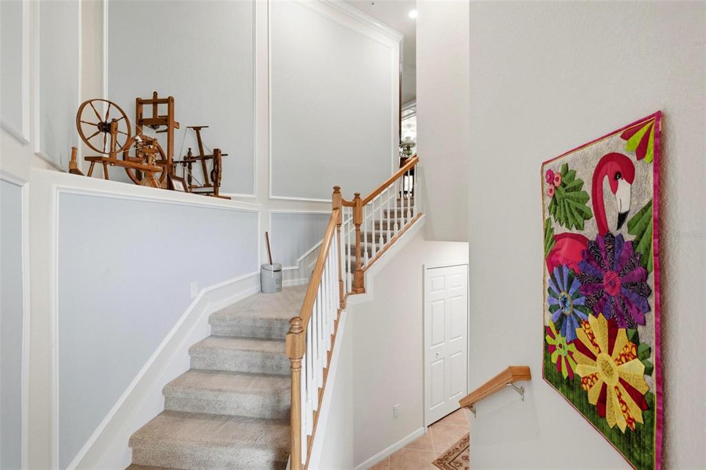 A carpeted staircase with wooden railings leads upward past a wall-mounted flamingo quilt — 20120 RAGAZZA CIRCLE UNIT 202, VENICE, FL