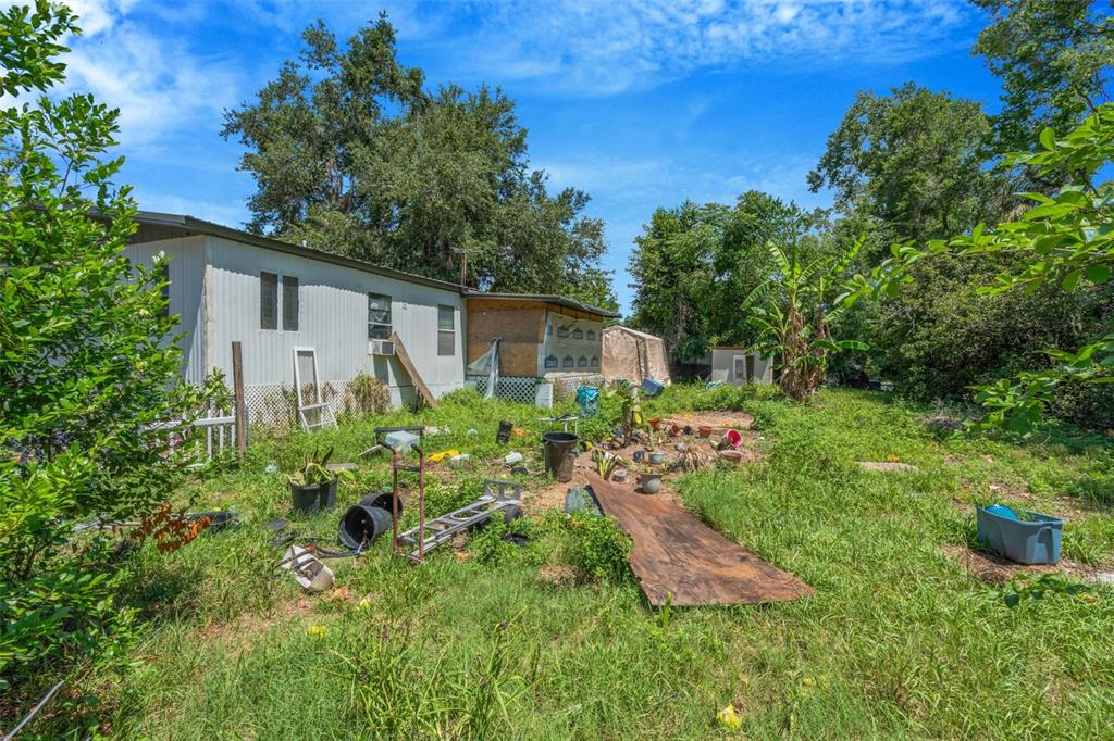 A view of the exterior of a mobile home with an overgrown, cluttered backyard — 35913 VALLEYBROOK AVENUE, ZEPHYRHILLS, FL