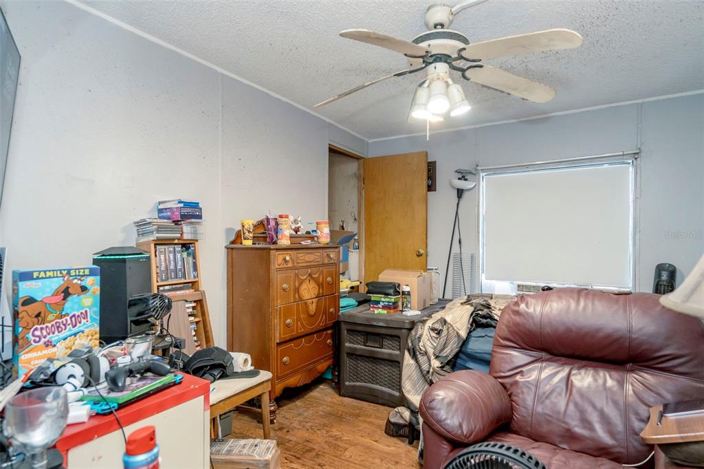 A cluttered bedroom features a ceiling fan, a leather recliner, a wooden dresser, and wood flooring — 35913 VALLEYBROOK AVENUE, ZEPHYRHILLS, FL