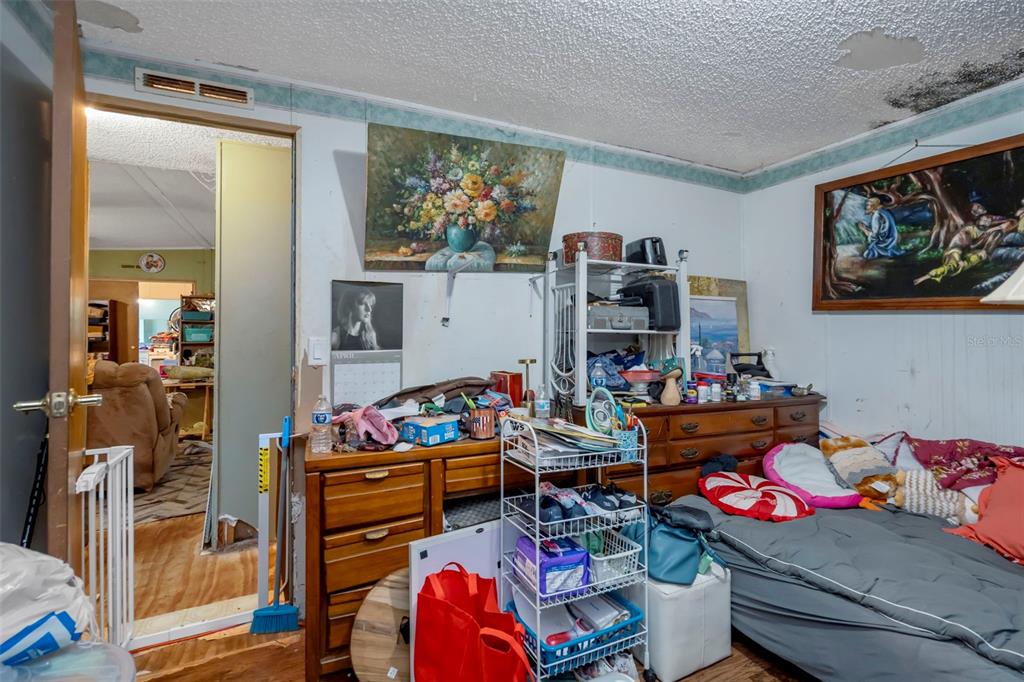 A cluttered bedroom with wood-paneled walls, a bed, a dresser, and visible ceiling water damage — 35913 VALLEYBROOK AVENUE, ZEPHYRHILLS, FL