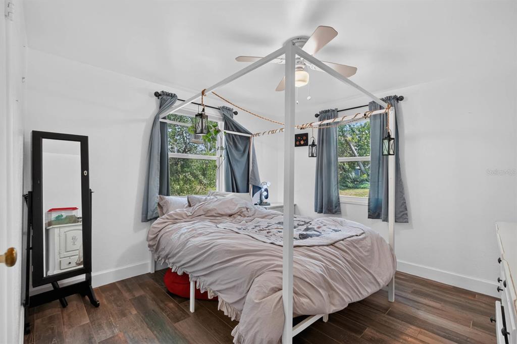 A bedroom features a white canopy bed, wood-look flooring, and two windows with blue curtains — 277 DEBARY DRIVE, DEBARY, FL
