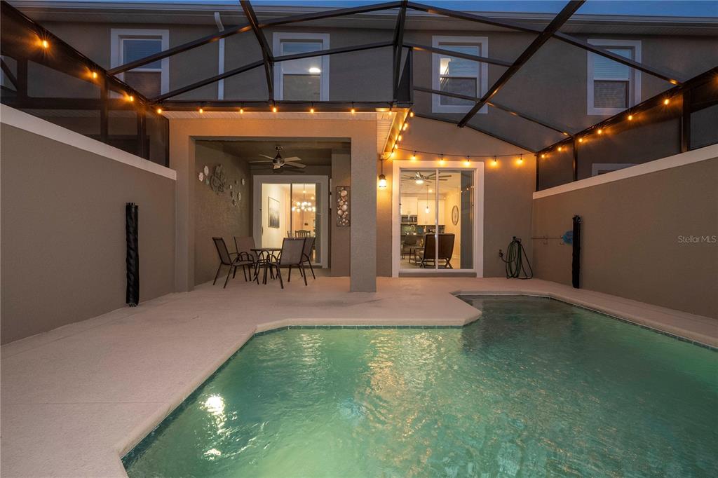 A screened-in patio features a swimming pool, outdoor dining furniture, and string lighting — 4399 SCENE LANE, KISSIMMEE, FL