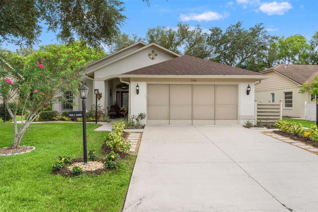 A single-story house with a beige stucco exterior, a two-car garage, and a landscaped yard — 7350 ROSEMONT LANE, SPRING HILL, FL