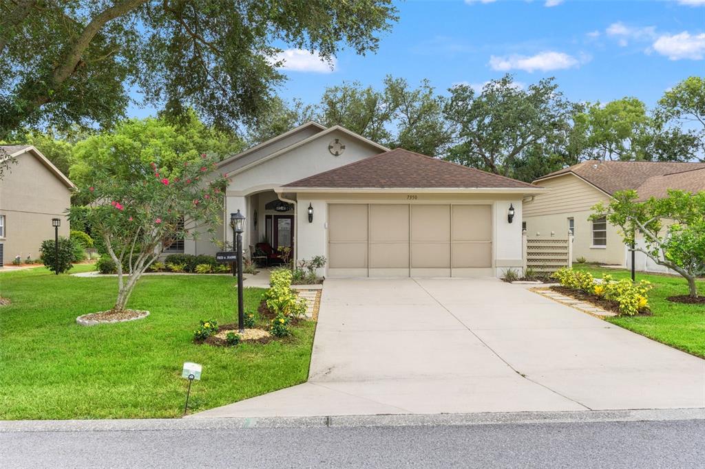A single-story house with a beige stucco exterior, a brown roof, and a concrete driveway — 7350 ROSEMONT LANE, SPRING HILL, FL