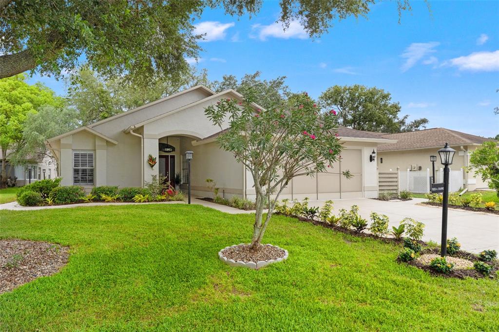 A single-story house with a beige stucco exterior, a two-car garage, and a landscaped lawn — 7350 ROSEMONT LANE, SPRING HILL, FL