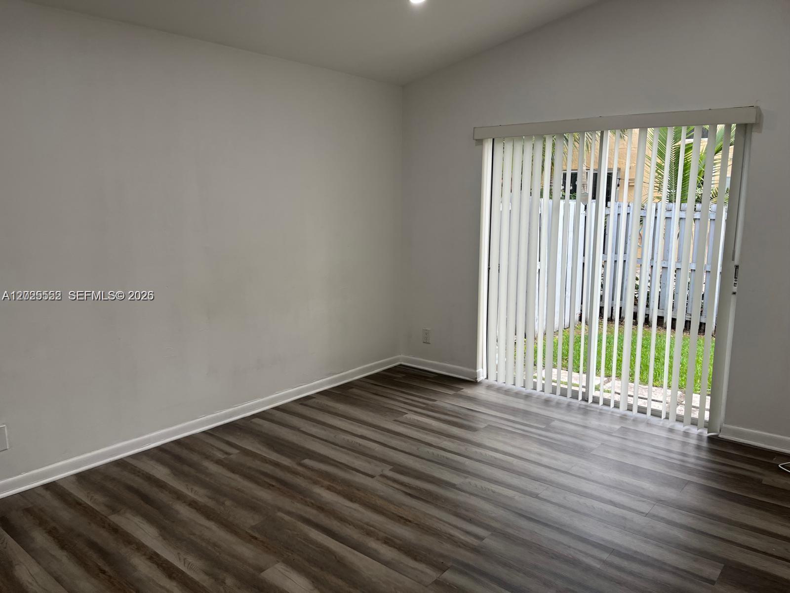 An empty room features light gray walls, wood-look flooring, and a sliding glass door — 1294 Seagrape Cir, Weston FL 33326, WESTON, FL