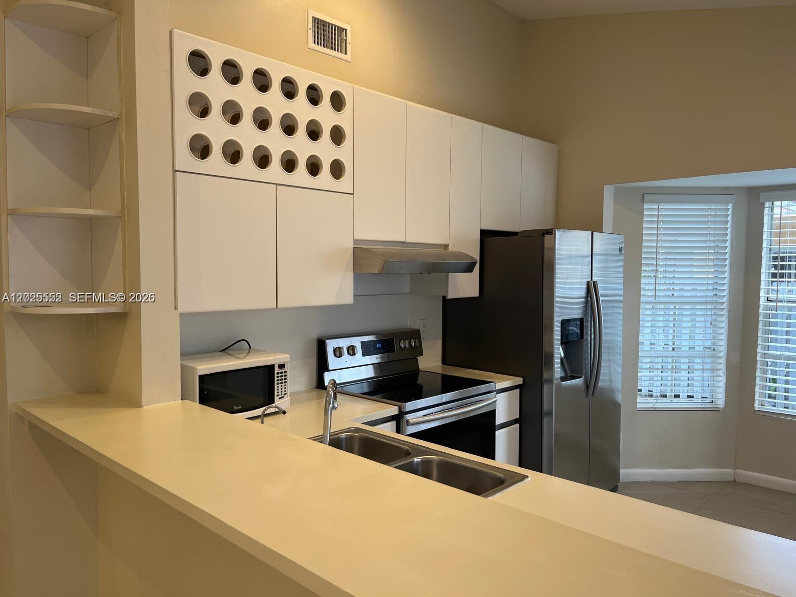 A kitchen features white cabinets, stainless steel appliances, a double sink, and a breakfast bar — 1294 Seagrape Cir, Weston FL 33326, WESTON, FL