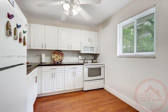 A kitchen features white cabinets, a white stove, a window, and wood-look flooring — 7703 Camino Real # A105, Miami FL 33143, MIAMI, FL