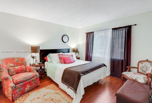 A bedroom features a bed, a floral armchair, a wooden chair, and a window with curtains — 7703 Camino Real # A105, Miami FL 33143, MIAMI, FL