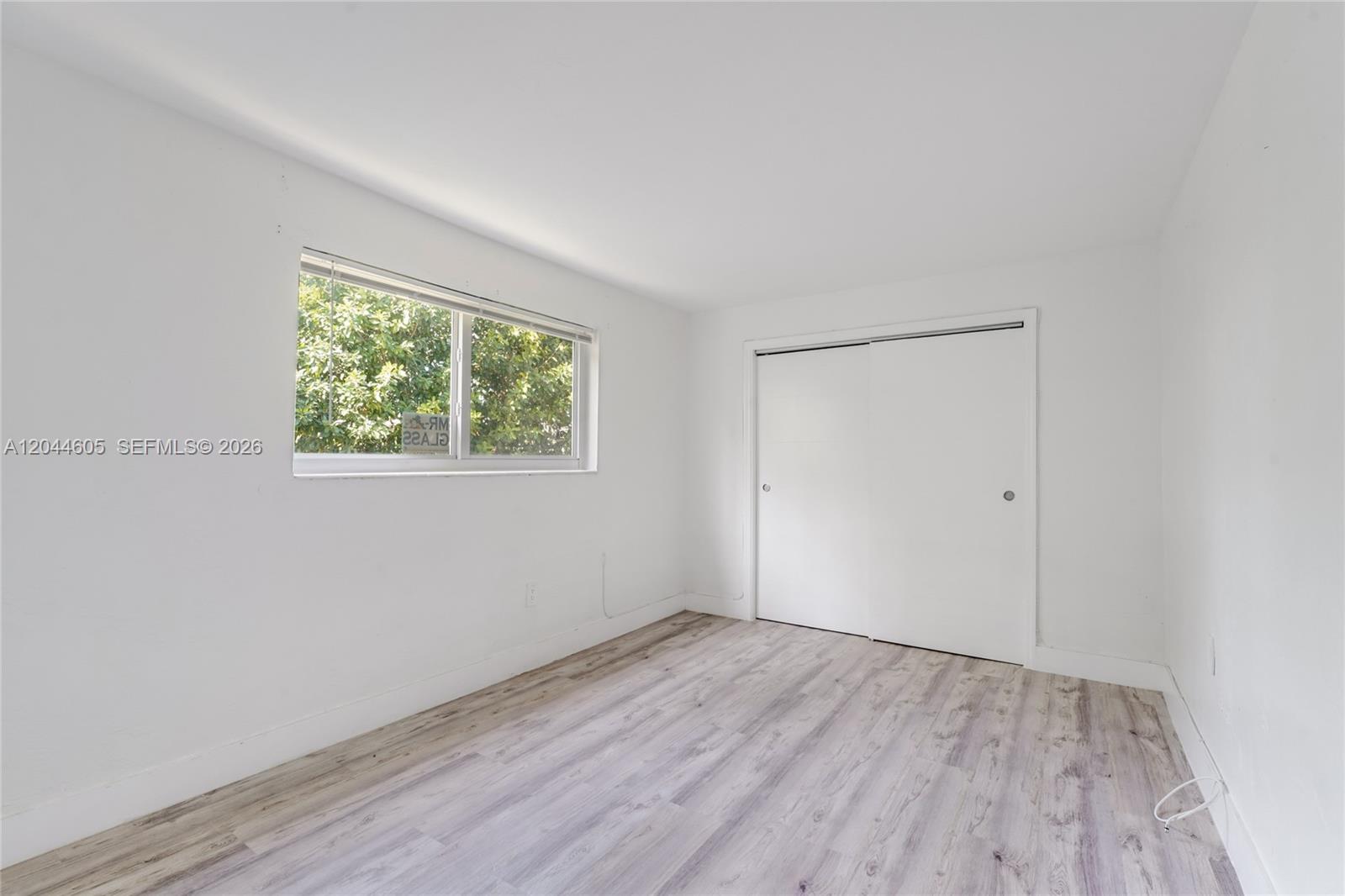An empty bedroom features white walls, light wood-look flooring, a window, and sliding closet doors — 1630 NW 18th St # 3, Miami FL 33125, MIAMI, FL