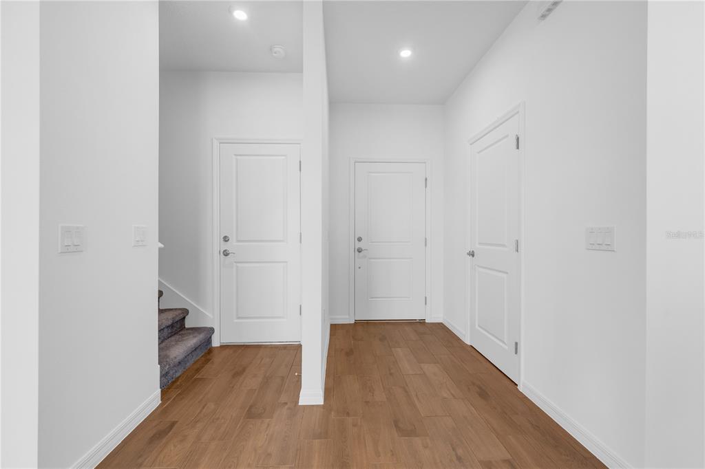 An interior view of a hallway with wood-look flooring, white walls, and three closed doors — 4437 RIVER BEACON BOULEVARD, DAVENPORT, FL