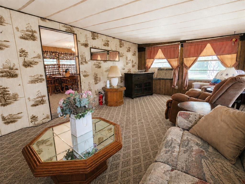 A living room features patterned wallpaper, a glass-topped coffee table, and brown reclining chairs — 9997 SE 167TH LANE, SUMMERFIELD, FL