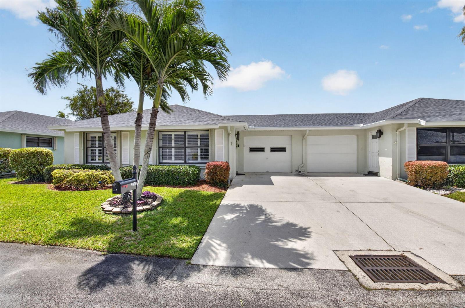 A single-story duplex with a concrete driveway, two garage doors, and palm trees in front — 9800 Tabebuia Tree Drive # A, Boynton Beach FL 33436, BOYNTON BEACH, FL