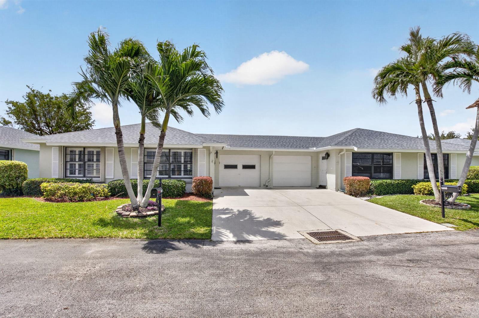 A single-story duplex with a shared driveway, two garage doors, and palm trees in front — 9800 Tabebuia Tree Drive # A, Boynton Beach FL 33436, BOYNTON BEACH, FL