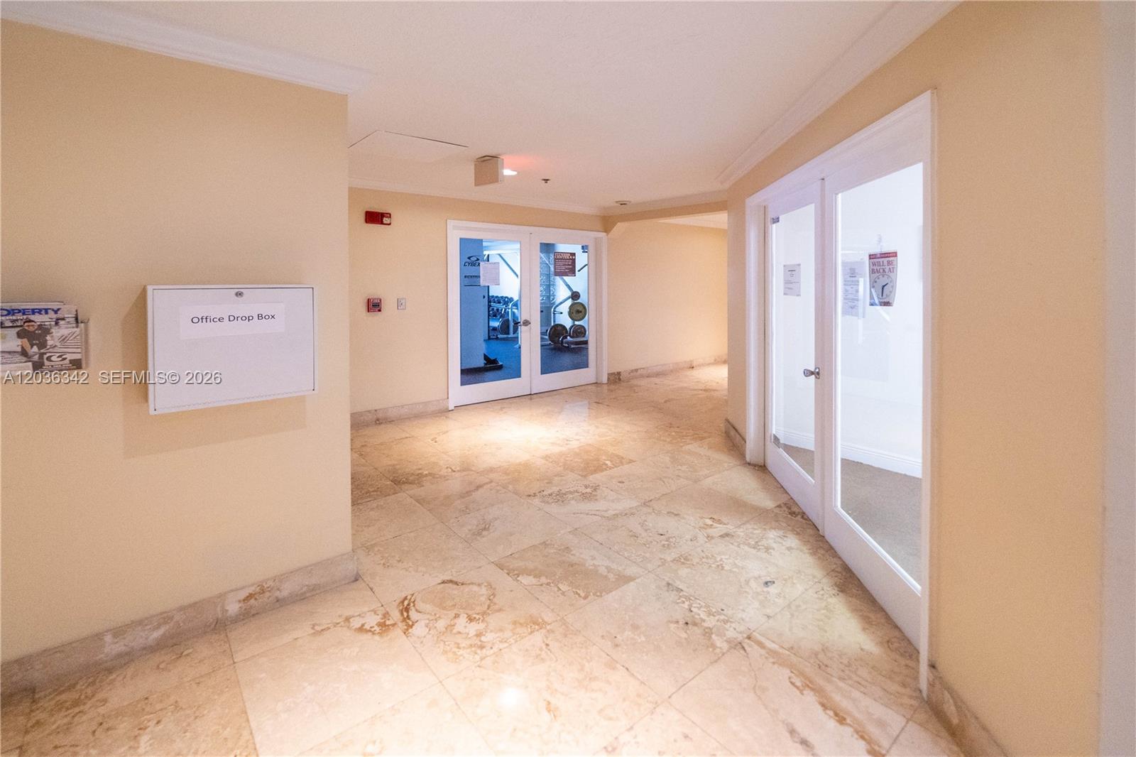 A hallway with tile flooring leads to a gym and a glass-paned office door — 1650 Coral Way # 507, Miami FL 33145, MIAMI, FL