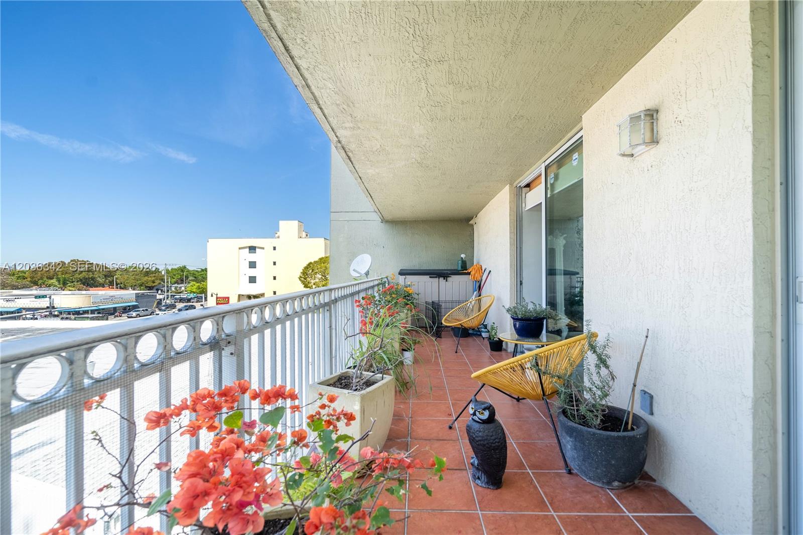 A balcony features terracotta tile flooring, yellow chairs, potted plants, and a metal railing — 1650 Coral Way # 507, Miami FL 33145, MIAMI, FL