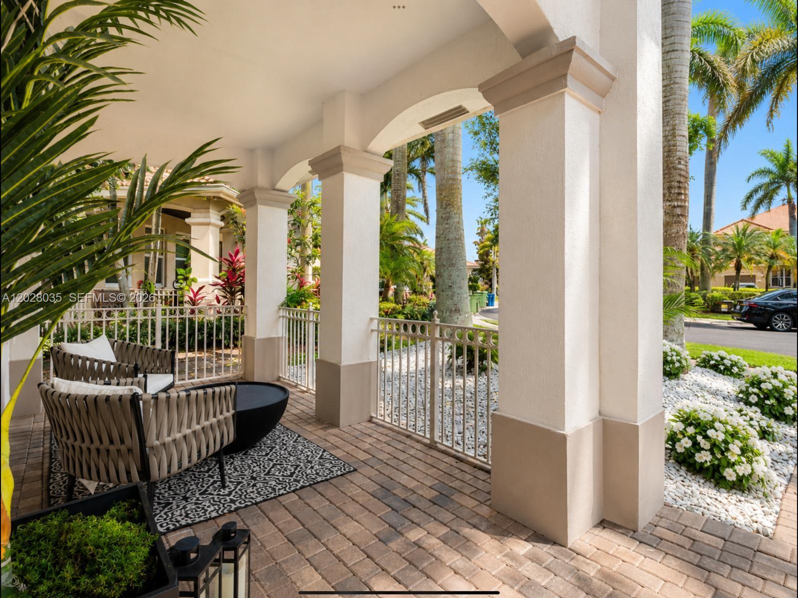 A covered patio features brick pavers, white columns, a metal railing, and outdoor seating — 1088 Skylark Dr, Weston FL 33327, WESTON, FL