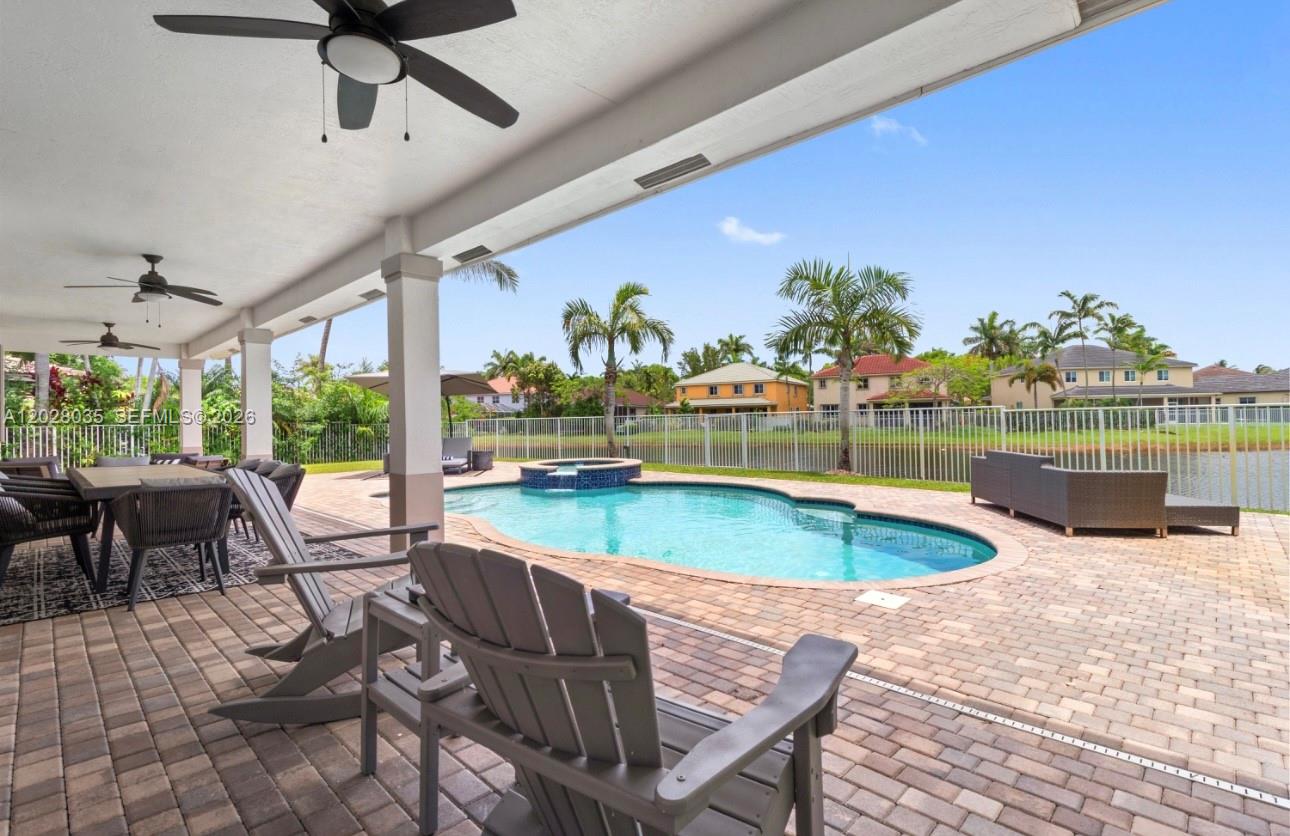A covered patio overlooks a swimming pool, spa, and a lake with houses beyond — 1088 Skylark Dr, Weston FL 33327, WESTON, FL