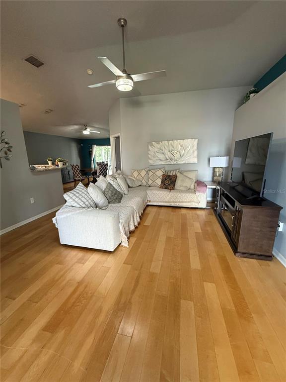 A living room features light wood flooring, a sectional sofa, and a television on a stand — 10707 PALAISEAU COURT, ORLANDO, FL