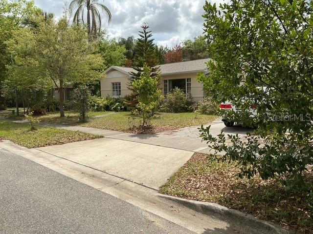 A single-story house with a concrete driveway and surrounding trees under a cloudy sky — 210 ALPINE DRIVE, MAITLAND, FL
