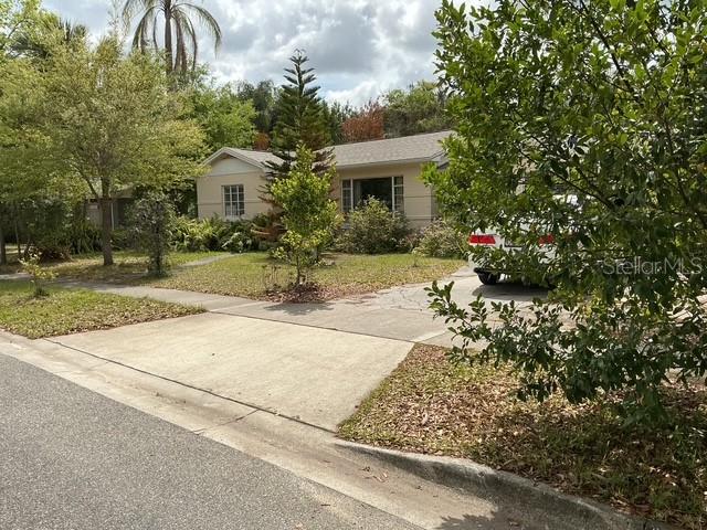 A single-story house with a concrete driveway and surrounding trees under a cloudy sky — 210 ALPINE DRIVE, MAITLAND, FL