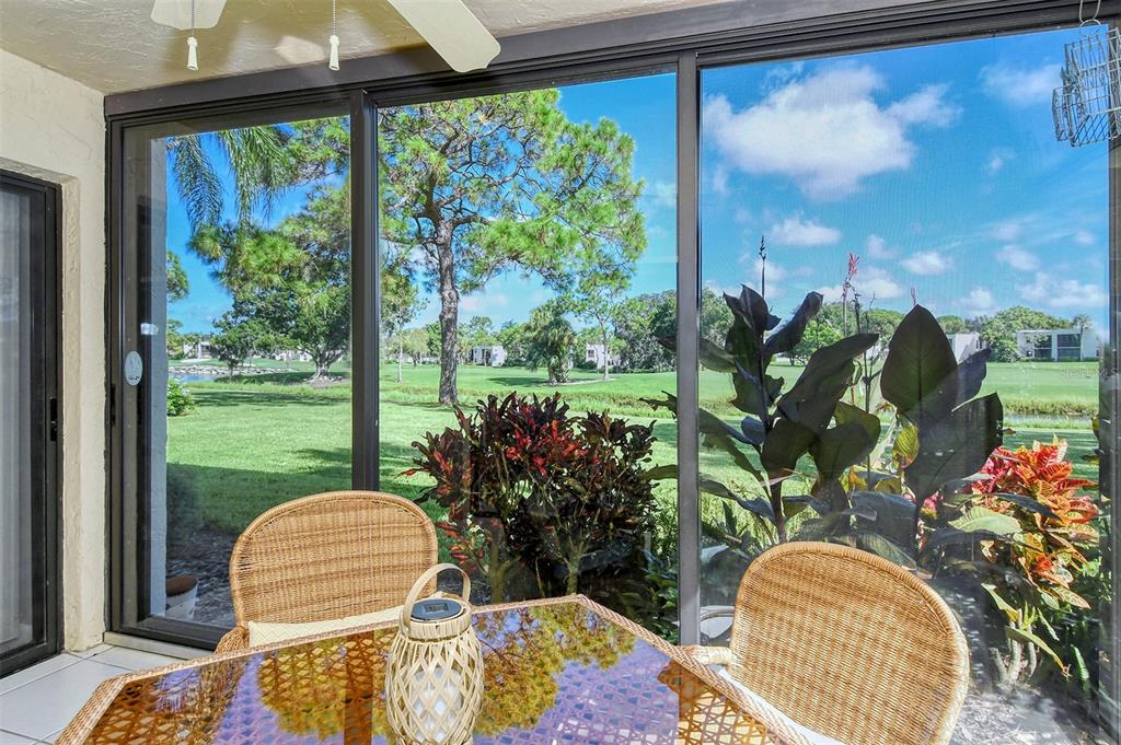 A sunroom with wicker chairs and a glass table overlooks a grassy lawn and trees — 5133 WILLOW LINKS UNIT 11, SARASOTA, FL