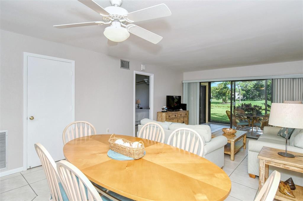 A dining area with a wooden table leads into a living room with sliding glass doors — 5133 WILLOW LINKS UNIT 11, SARASOTA, FL