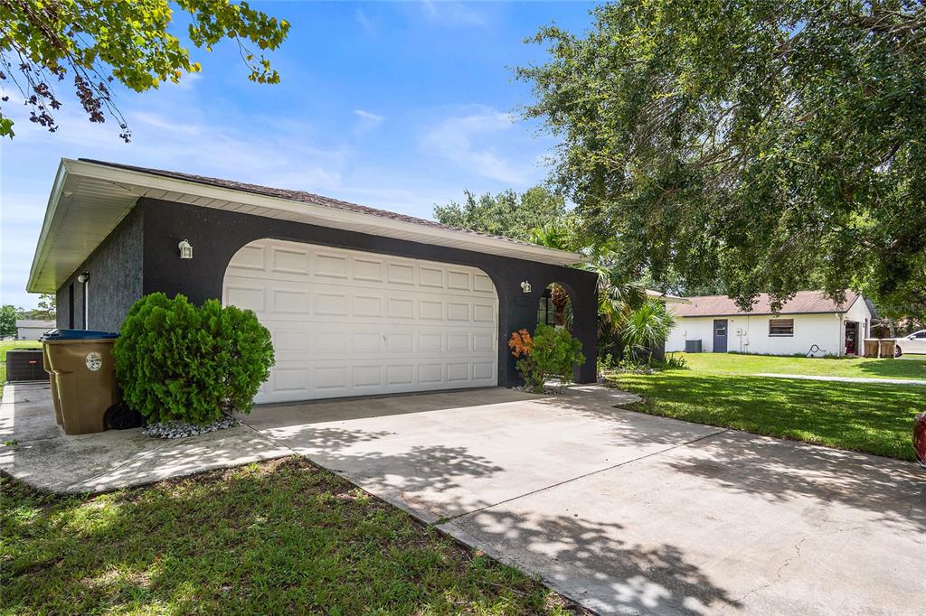 A dark-colored garage with a white door and a concrete driveway under a large tree — 1177 LIZA STREET, ST CLOUD, FL