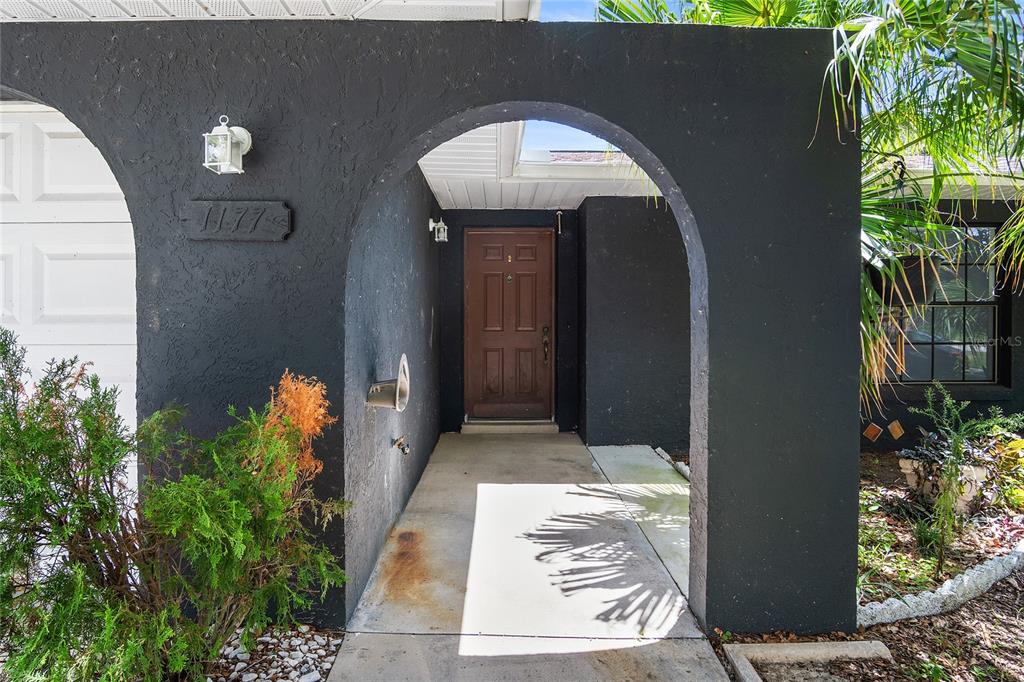 A dark-painted exterior entryway features an arched opening, a brown door, and house number 1177 — 1177 LIZA STREET, ST CLOUD, FL