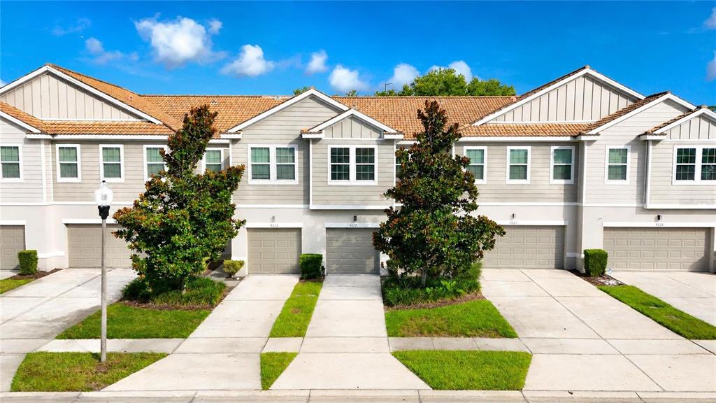 A row of light-colored townhouses features beige garage doors and manicured green lawns — 9217 SHEPTON STREET, ORLANDO, FL