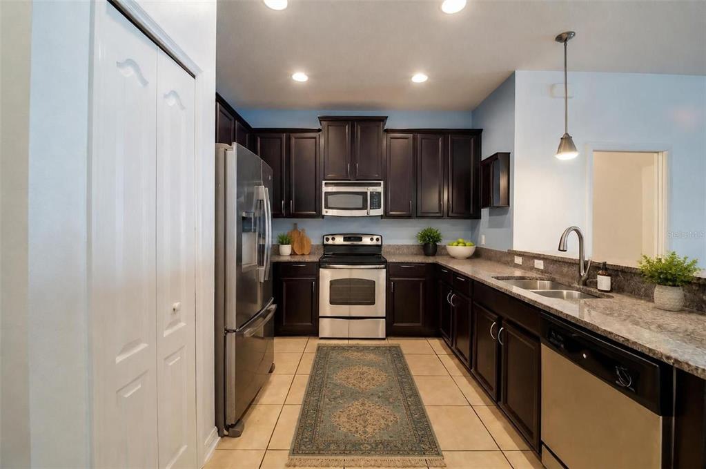 A kitchen features dark wood cabinets, stainless steel appliances, granite countertops, and a tile floor — 9217 SHEPTON STREET, ORLANDO, FL
