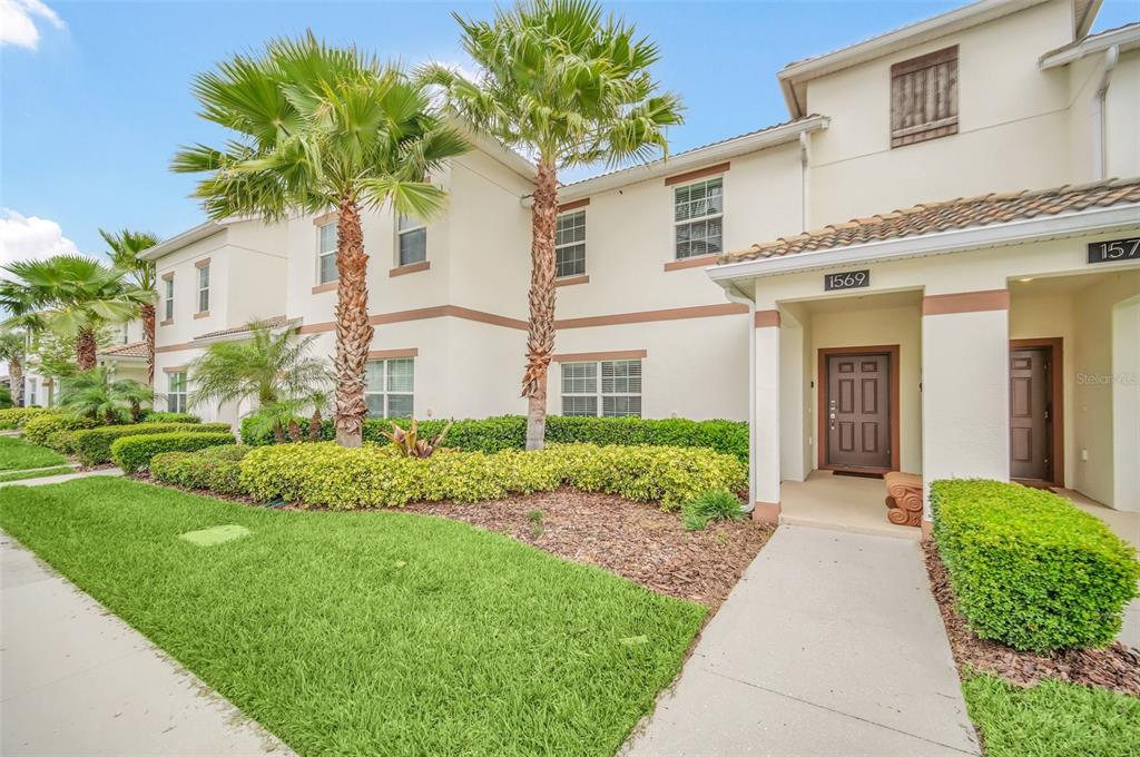 A two-story townhouse exterior with a tan stucco facade, palm trees, and a concrete walkway — 1569 PLUNKER DRIVE, DAVENPORT, FL