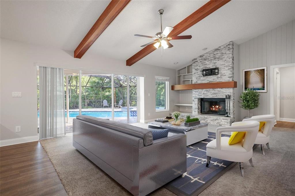 A living room features a stone fireplace, wood ceiling beams, and sliding doors to a pool — 3297 VALEMOOR DRIVE, PALM HARBOR, FL