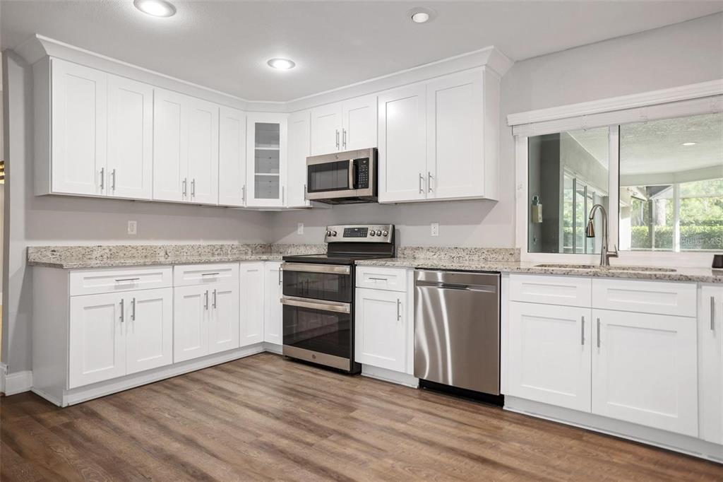 A kitchen with white cabinets, stainless steel appliances, granite countertops, and wood-look flooring — 3297 VALEMOOR DRIVE, PALM HARBOR, FL