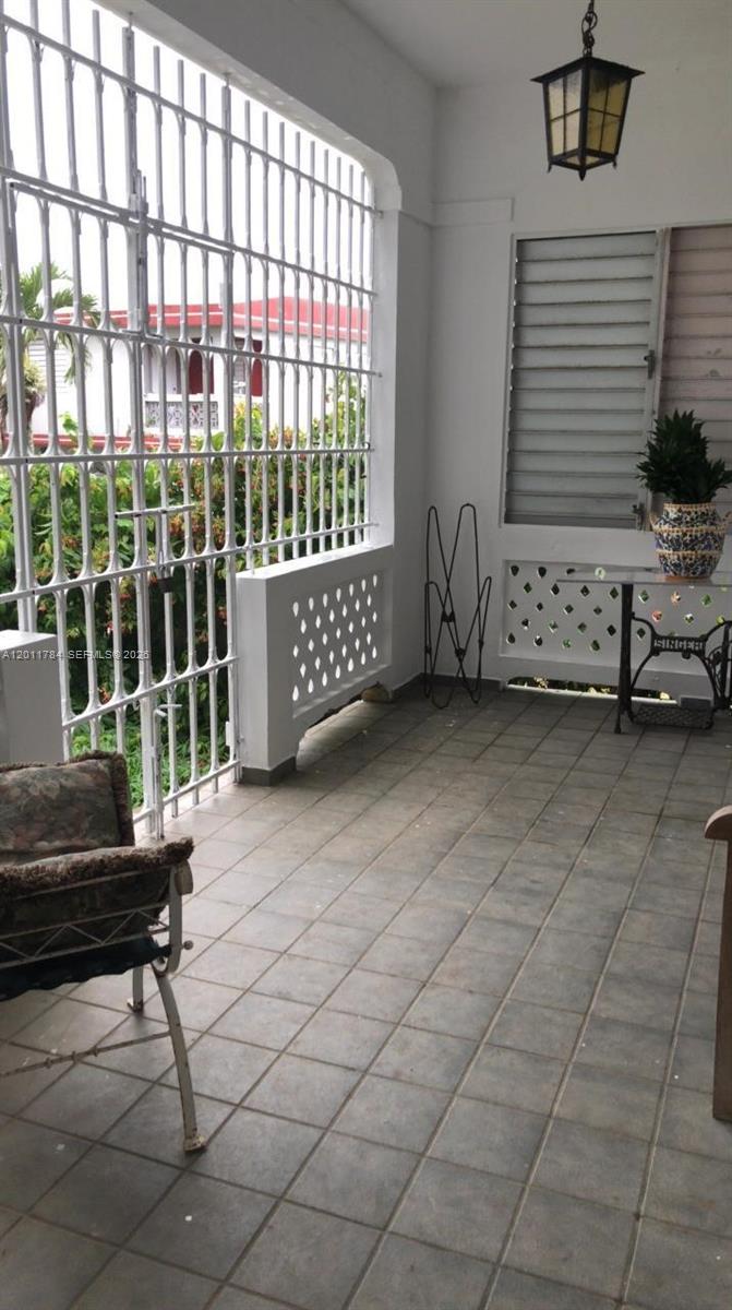 A tiled porch features a white metal security gate, a hanging lantern, and a Singer table — - Padial Sur #171 Aibonito, PR 00705, PR
