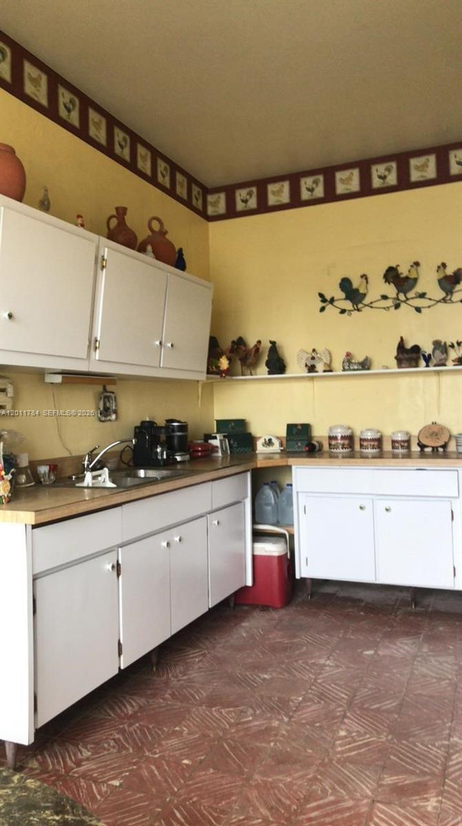 A kitchen features white cabinets, yellow walls with rooster-themed decor, and patterned tile flooring — - Padial Sur #171 Aibonito, PR 00705, PR