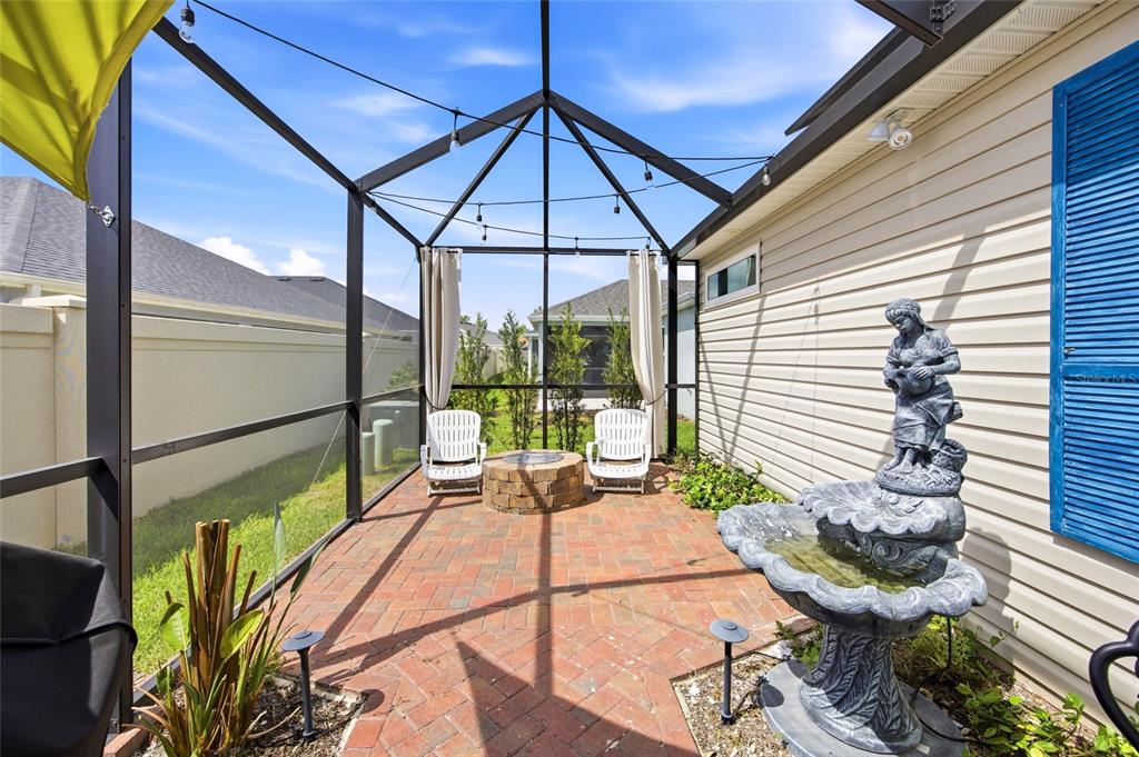 A screened-in brick patio features a stone fire pit, two chairs, and a tiered fountain — 2910 MONUMENT WAY, THE VILLAGES, FL