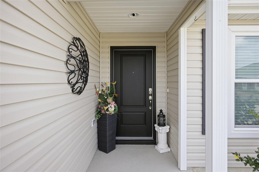 A black front door sits under a covered porch with beige siding and a planter — 2910 MONUMENT WAY, THE VILLAGES, FL