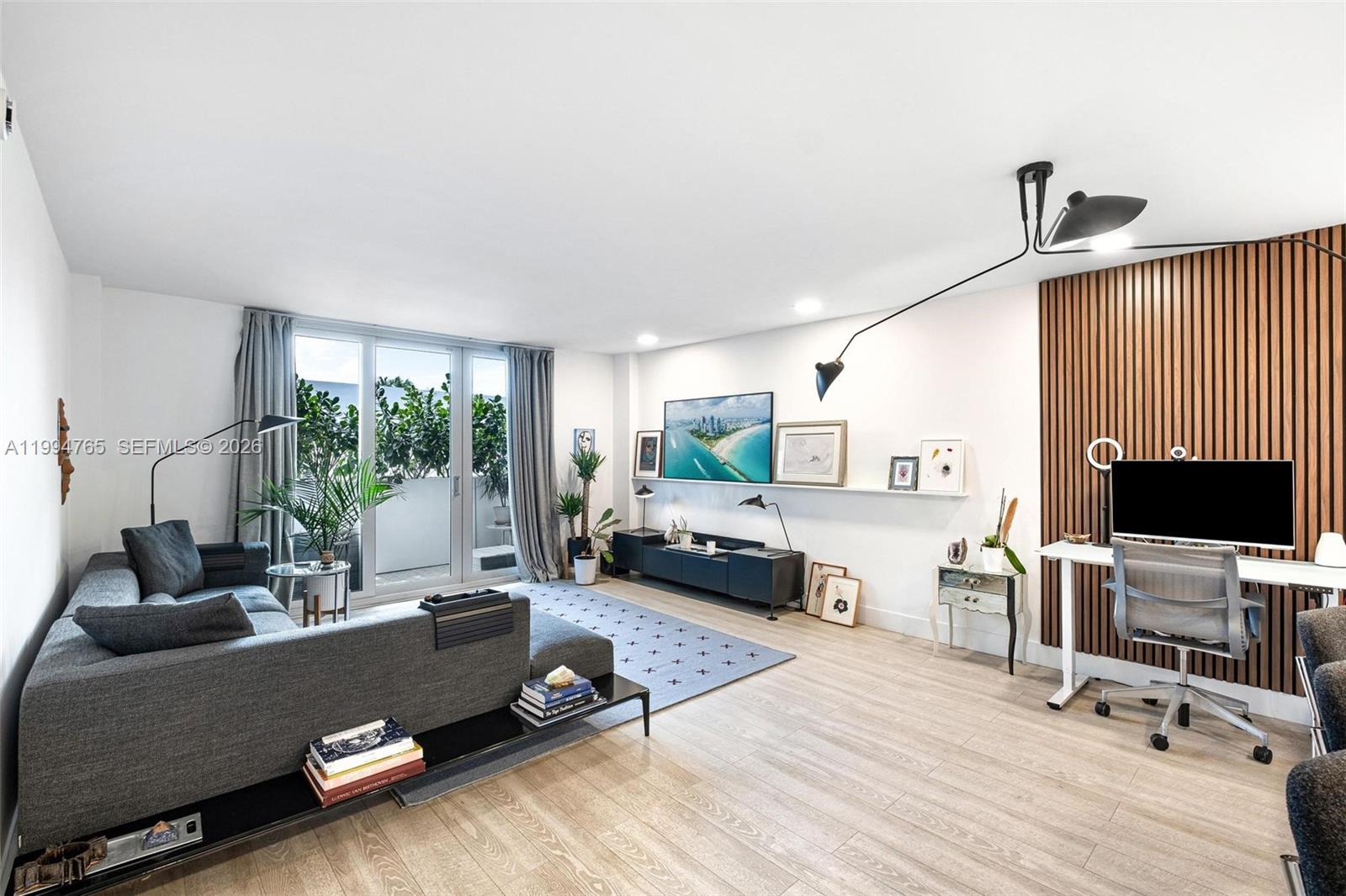 A modern living room features a gray sectional sofa, a workspace with wood-slat wall paneling, and a balcony — 5 Island Ave, Miami Beach FL 33139, MIAMI BEACH, FL