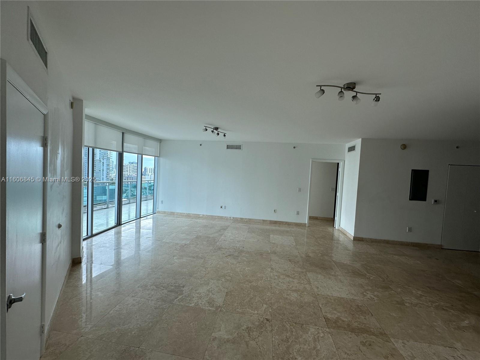 An empty living room features beige tile flooring, white walls, and floor-to-ceiling windows — 350 S Miami Ave # 2302, Miami FL 33130, MIAMI, FL