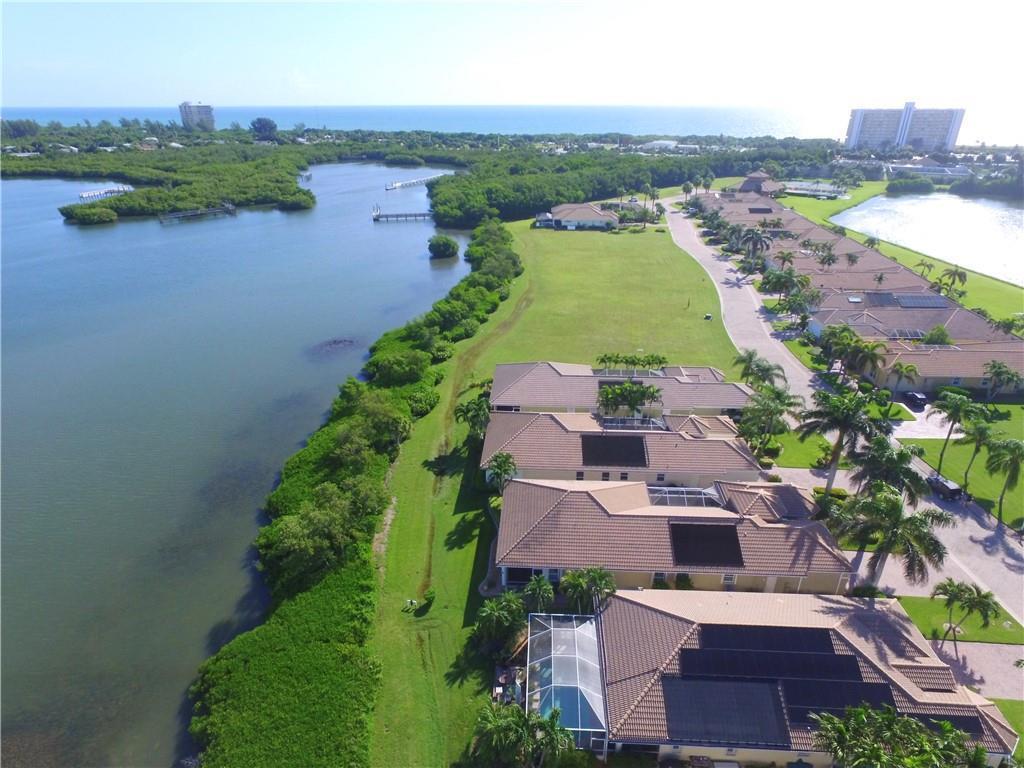An aerial view shows a row of waterfront townhomes with pools along a grassy shoreline — HUTCHINSON ISLAND, FL