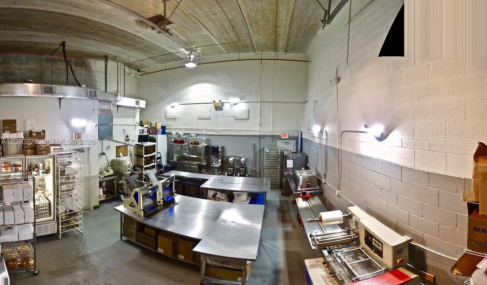 A commercial kitchen features stainless steel work tables, industrial equipment, and white block walls — 1365 NW 98th Ct, Doral FL 33172, DORAL, FL